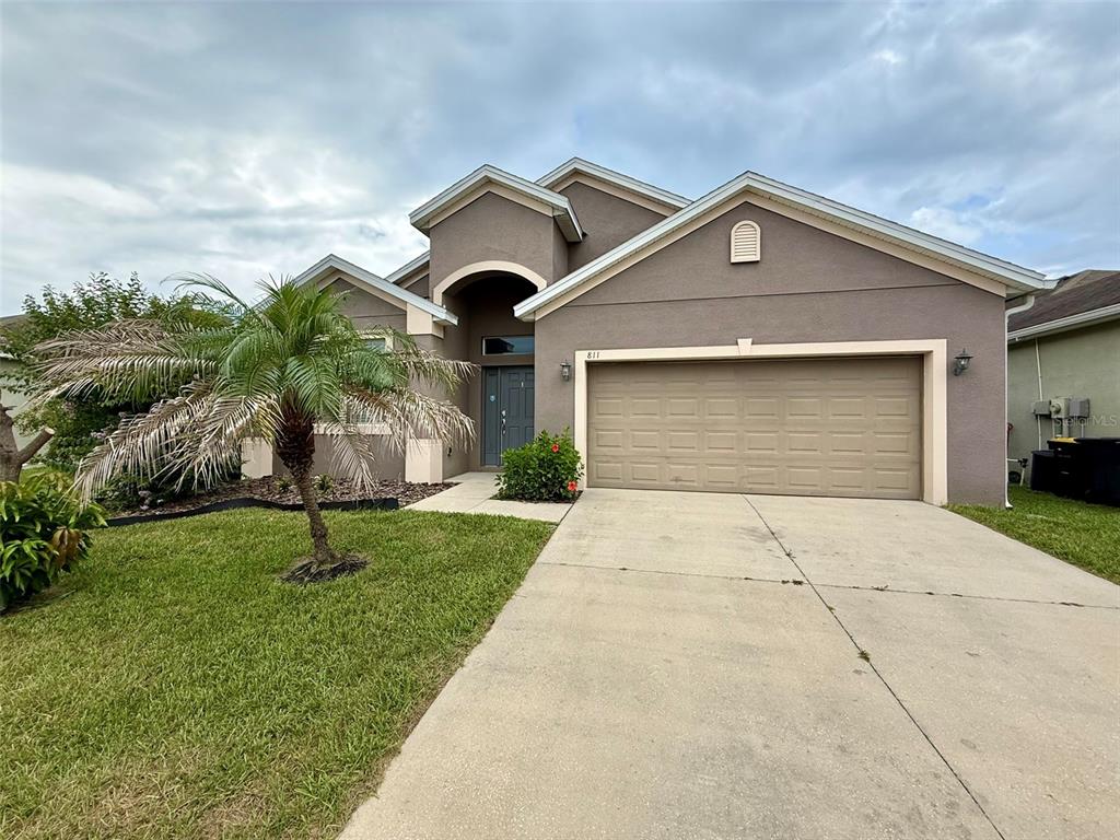 A single-story house with a tan stucco exterior, a two-car garage, and a palm tree — 811 KRENSON WOODS LANE, LAKELAND, FL