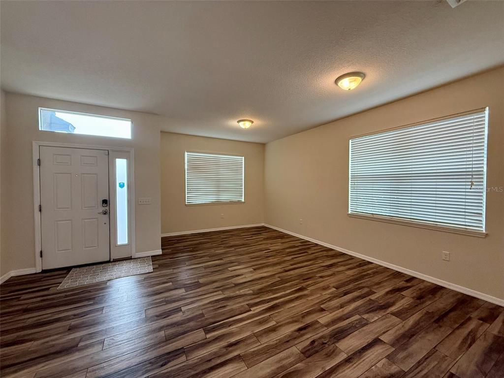 An empty living room features wood-look flooring, beige walls, and two windows with blinds — 811 KRENSON WOODS LANE, LAKELAND, FL