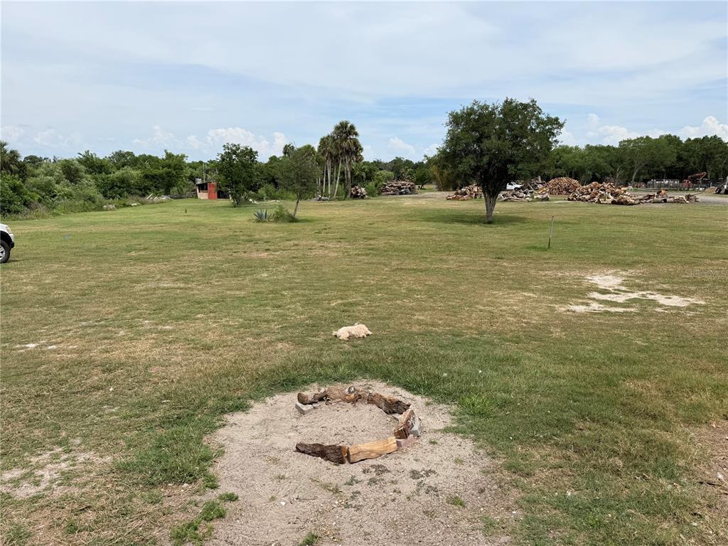 A grassy field features a fire pit made of logs and a small dog resting — 3208 16TH AVE E, PALMETTO, FL