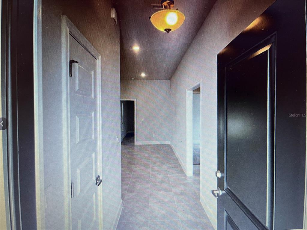 A hallway with light-colored tile flooring leads to multiple doorways under a ceiling light fixture — 16253 SE 83RD COURT, SUMMERFIELD, FL