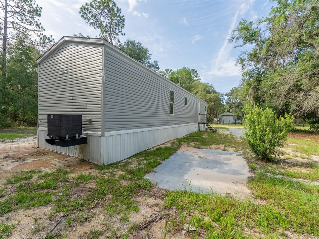 A long, gray mobile home sits on a sandy lot with an exterior HVAC unit — 14585 NE 149TH LANE, FORT MC COY, FL