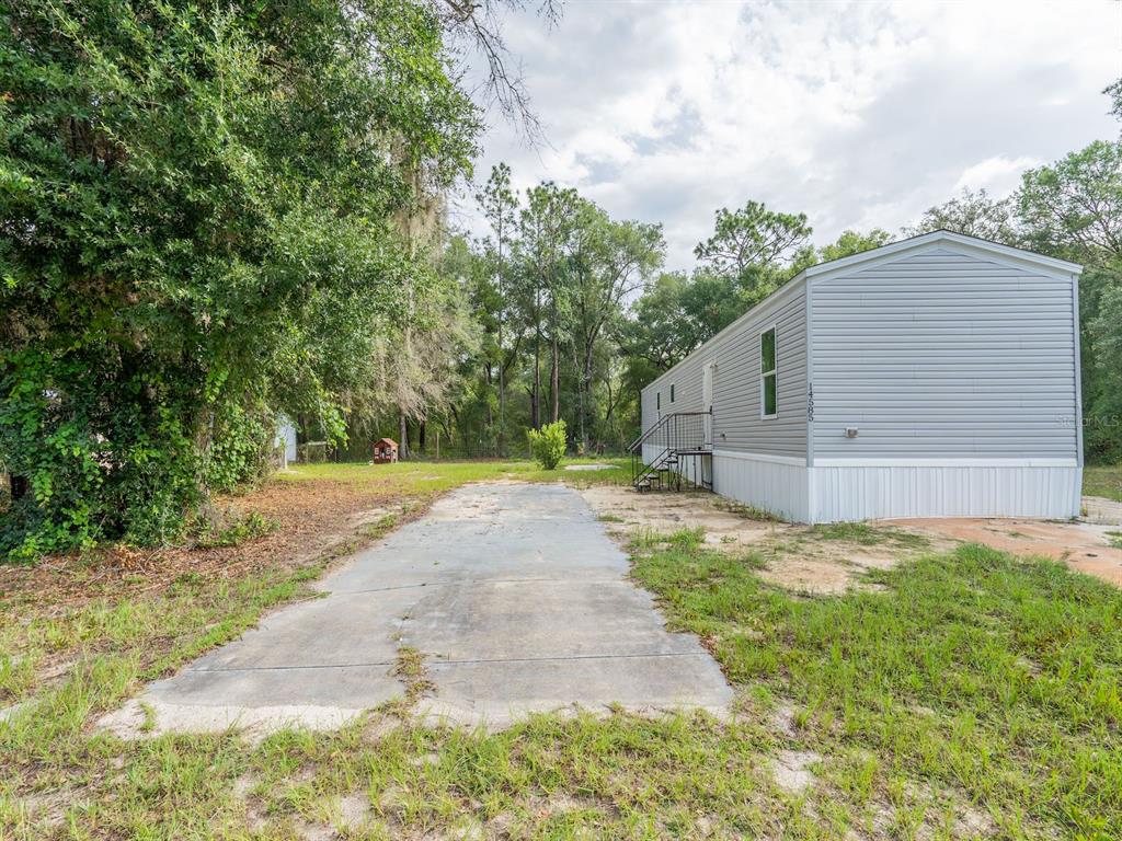 A gray manufactured home sits on a lot with a concrete driveway and trees — 14585 NE 149TH LANE, FORT MC COY, FL