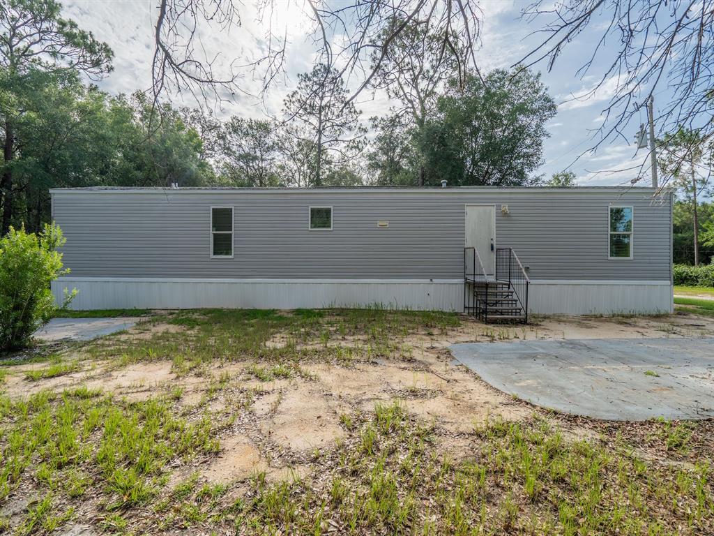 A gray mobile home with a white door and metal stairs sits on a dirt lot — 14585 NE 149TH LANE, FORT MC COY, FL