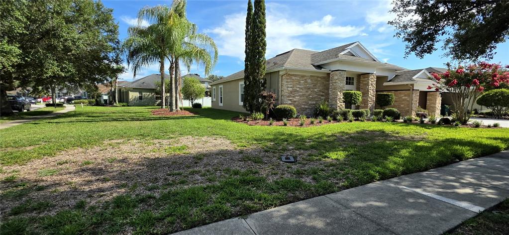 A single-story house with a stone facade and a large front lawn under a blue sky — 25638 FERDINAND COURT, WESLEY CHAPEL, FL