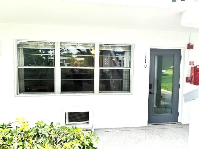 A white exterior wall features a large window, a wall-mounted air conditioner, and a door — 110 Markham F # 110, Deerfield Beach FL 33442, DEERFIELD BEACH, FL