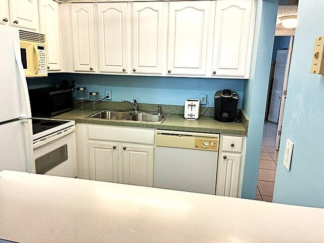 A kitchen features white cabinets, light countertops, a double sink, and a white dishwasher — 110 Markham F # 110, Deerfield Beach FL 33442, DEERFIELD BEACH, FL