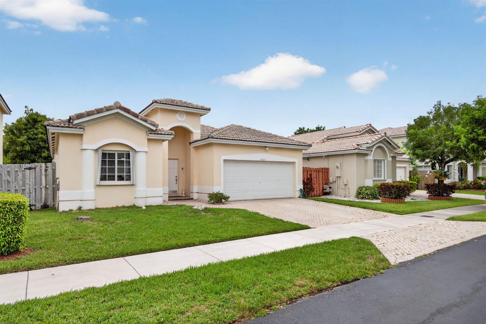 A single-story suburban house with a beige stucco exterior, tiled roof, and two-car garage — 14215 SW 156th Avenue N, Miami FL 33196, MIAMI, FL