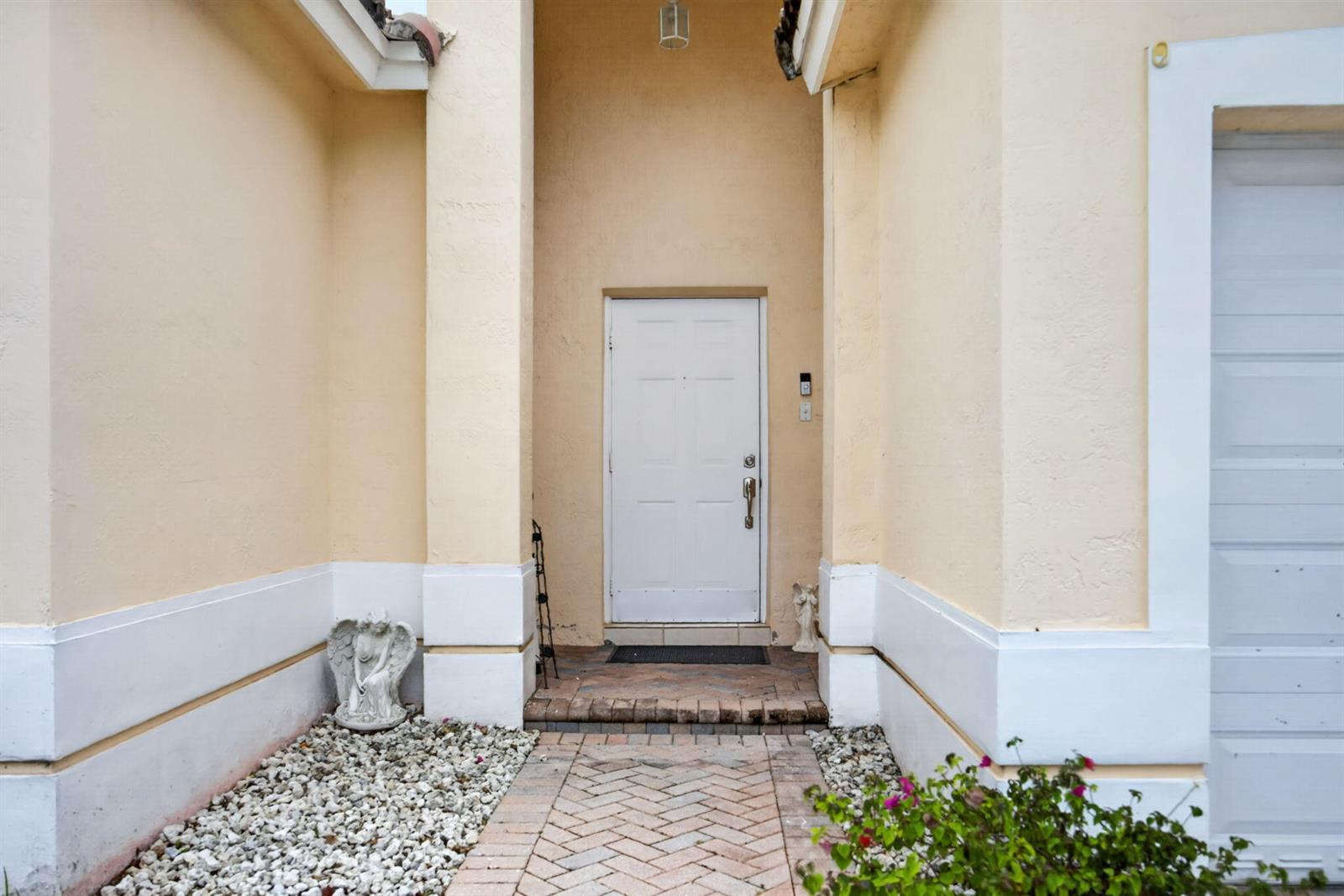 A white front door is centered between two beige walls with a brick walkway — 14215 SW 156th Avenue N, Miami FL 33196, MIAMI, FL