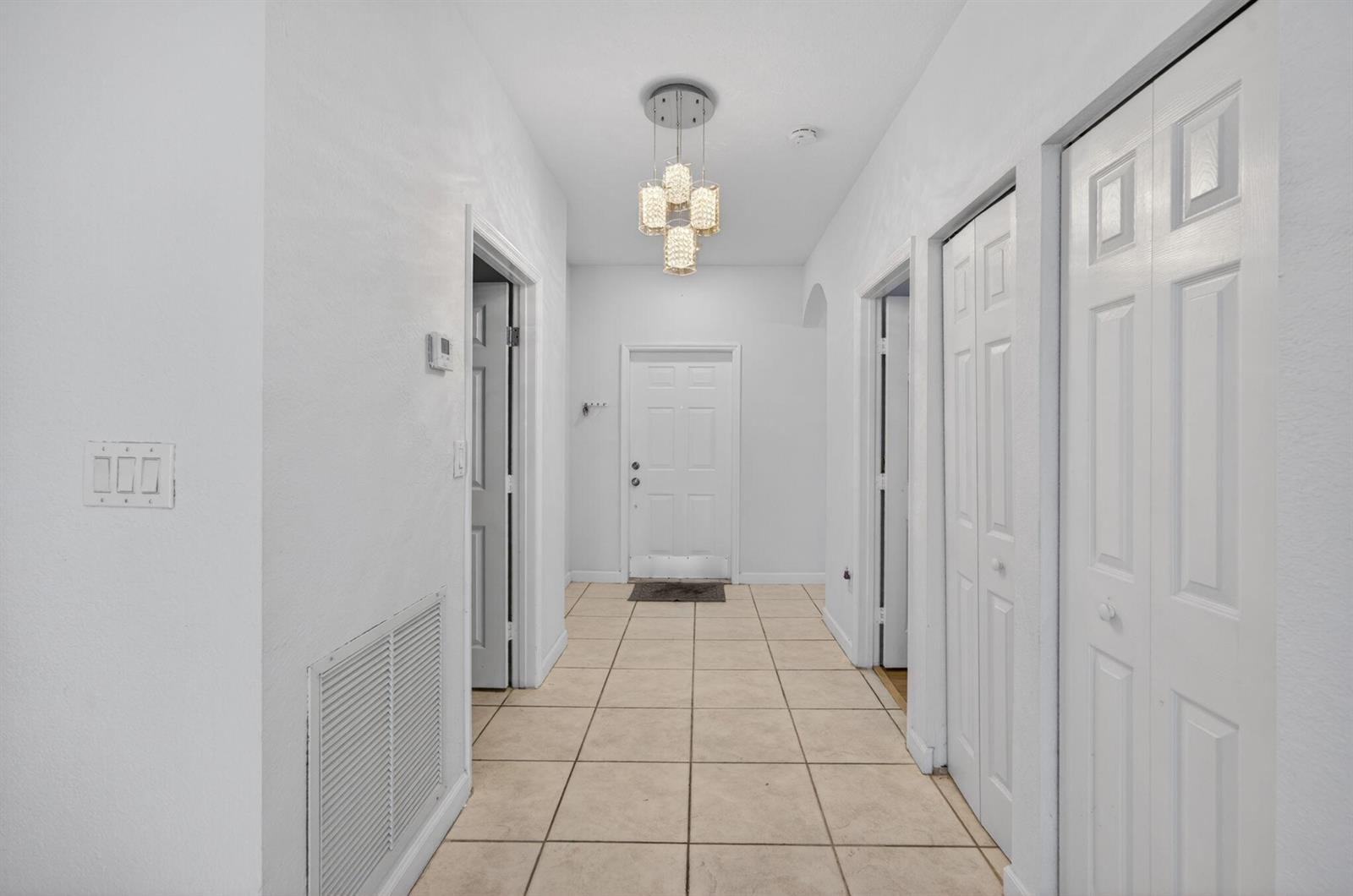 A hallway with white walls, tile flooring, a modern chandelier, and several white interior doors — 14215 SW 156th Avenue N, Miami FL 33196, MIAMI, FL