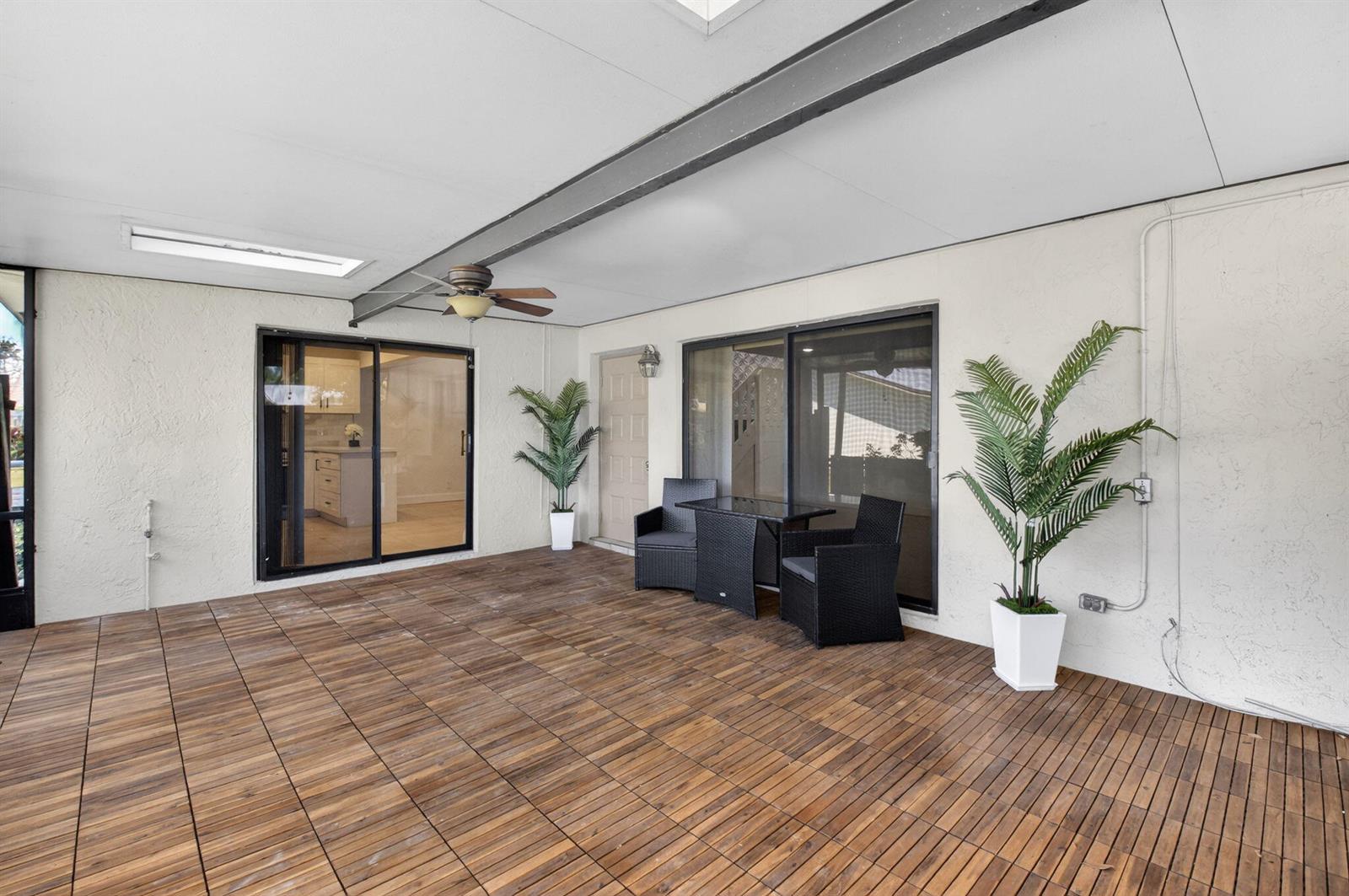 A covered patio features wood-look deck tiles, a ceiling fan, and black wicker patio furniture — 717 NW 29th Avenue # B, Delray Beach FL 33445, DELRAY BEACH, FL