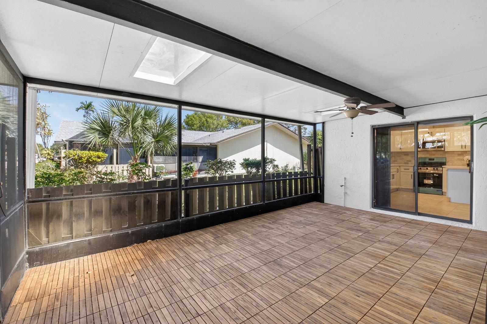 A covered patio with wood-look flooring, screen walls, a ceiling fan, and a sliding glass door — 717 NW 29th Avenue # B, Delray Beach FL 33445, DELRAY BEACH, FL