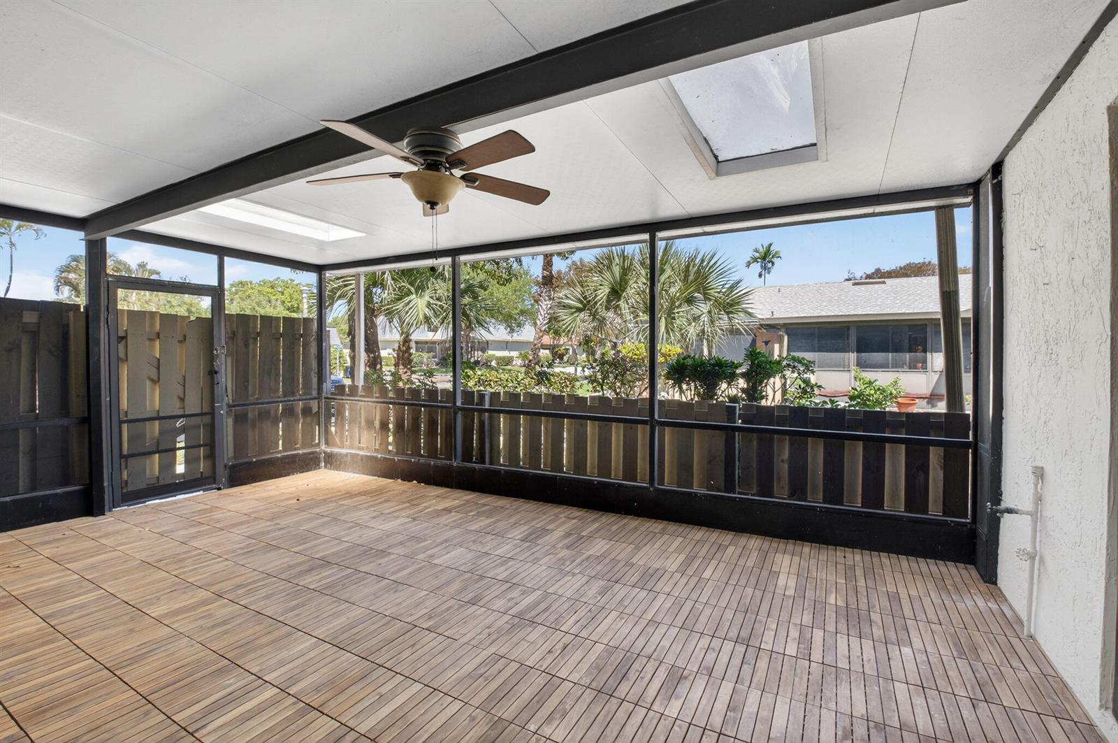A screened-in patio features wood-look flooring, a ceiling fan, and a view of a fence — 717 NW 29th Avenue # B, Delray Beach FL 33445, DELRAY BEACH, FL