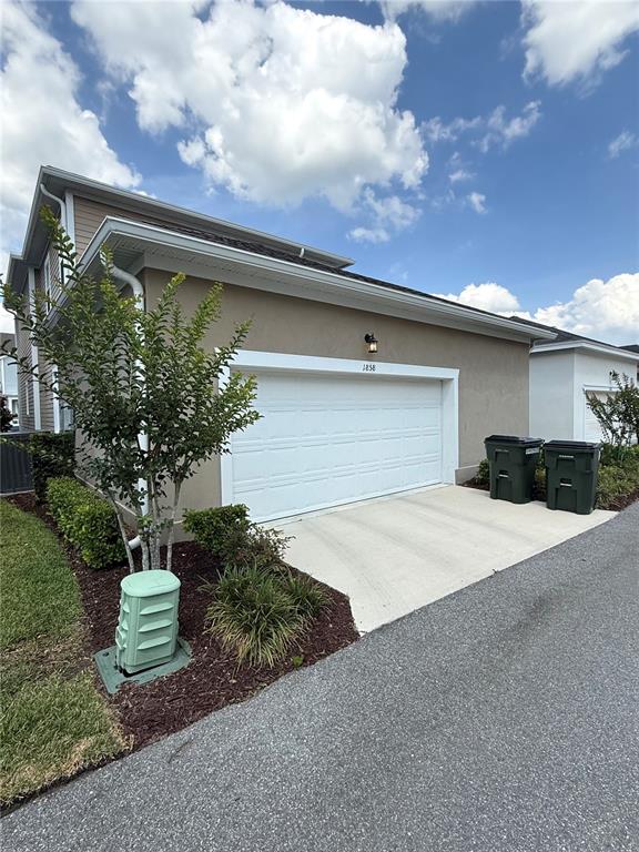 A tan house exterior features a white garage door, two trash bins, and landscaping — 1858 TREASURE COVE, CELEBRATION, FL