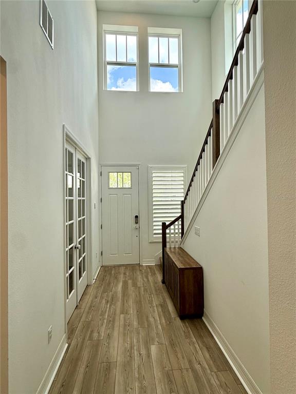 A bright entryway features a staircase, wood-look flooring, a front door, and double glass doors — 1858 TREASURE COVE, CELEBRATION, FL