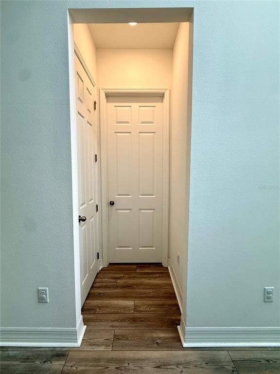 A hallway with wood-look flooring leads to a white door between two walls — 1858 TREASURE COVE, CELEBRATION, FL