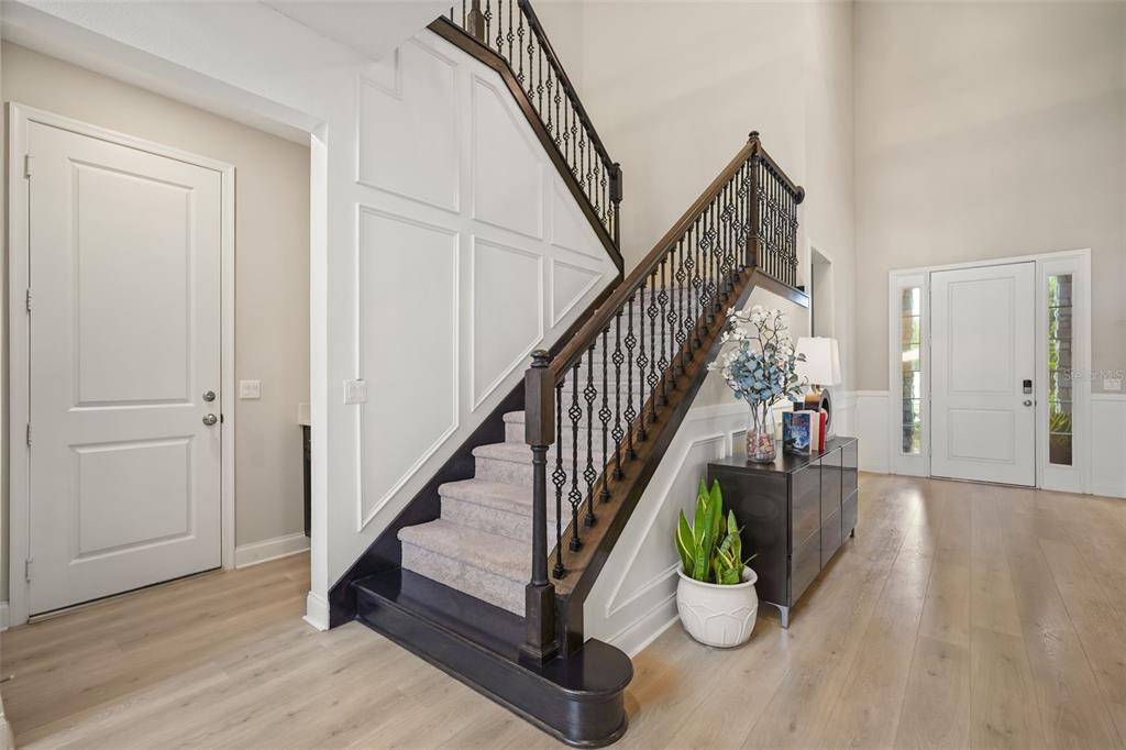 A staircase with dark wood railings and carpeted steps sits in a bright, modern entryway — 10713 BELLE MAISONS DRIVE, ORLANDO, FL