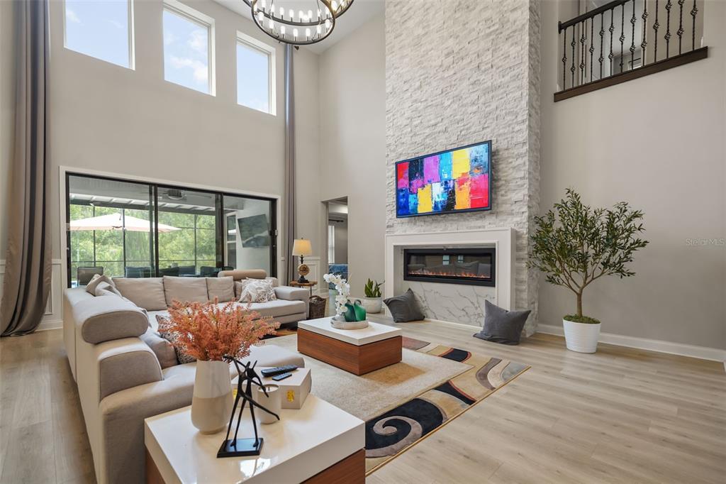 A living room features a tall stone fireplace, a large sectional sofa, and floor-to-ceiling windows — 10713 BELLE MAISONS DRIVE, ORLANDO, FL