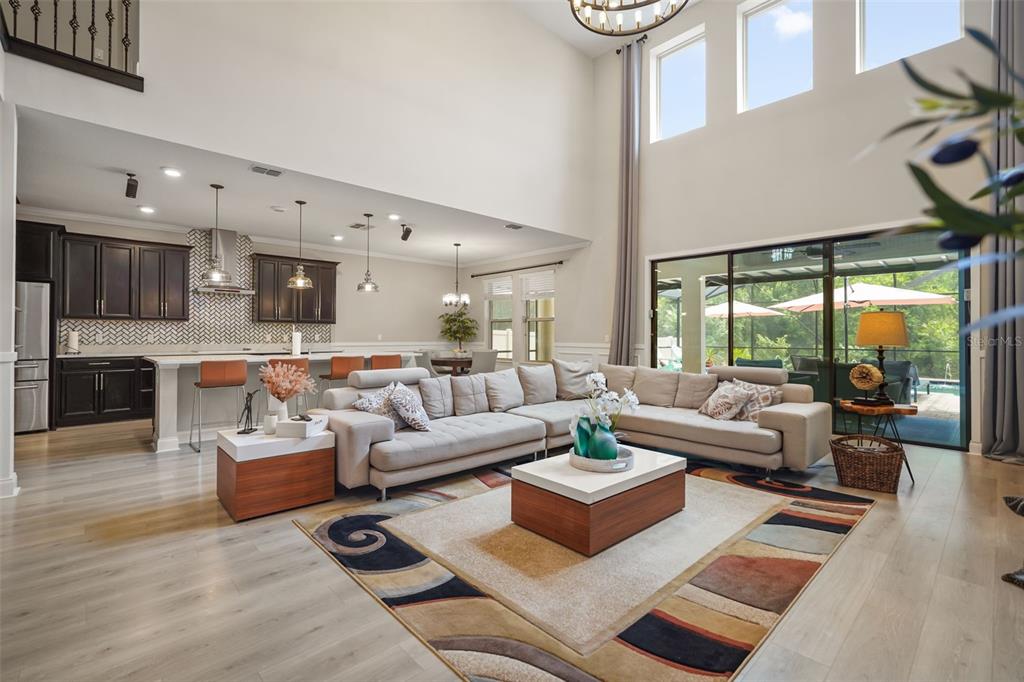 A spacious open-concept living room and kitchen featuring high ceilings, light wood floors, and furniture — 10713 BELLE MAISONS DRIVE, ORLANDO, FL