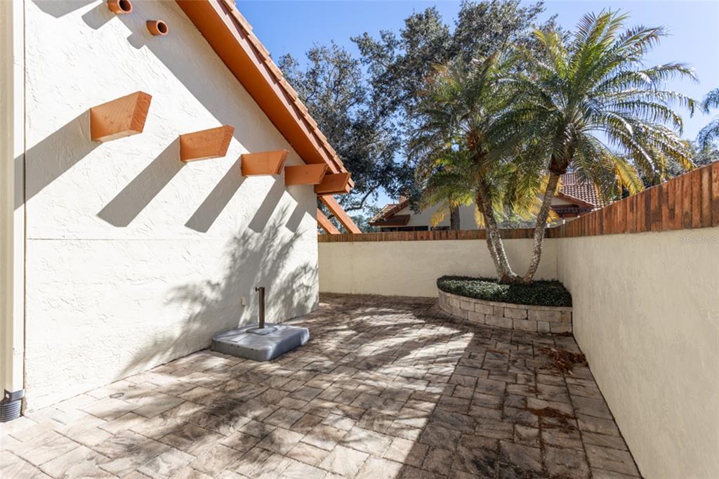 A paved patio area features a stucco wall with wooden rafters and a small palm tree — 39 VILLAGE CIRCLE UNIT 5-501, PALM COAST, FL