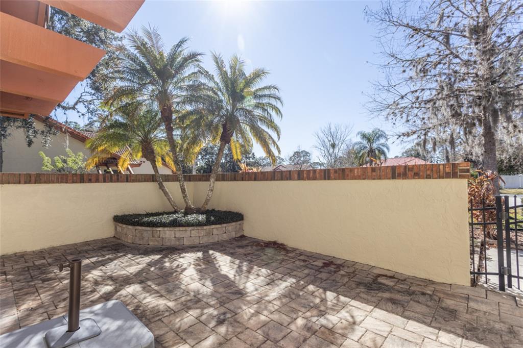 A paved patio features a raised planter with palm trees against a stucco wall — 39 VILLAGE CIRCLE UNIT 5-501, PALM COAST, FL