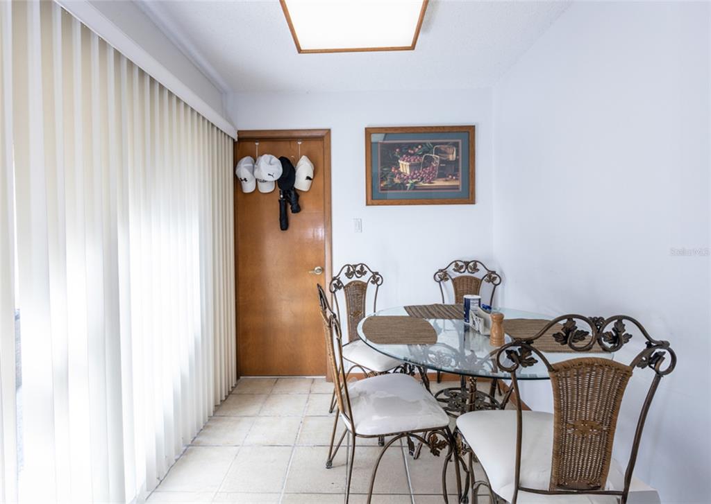 A dining area features a glass-topped table, wicker chairs, tiled floors, and a wooden door — 39 VILLAGE CIRCLE UNIT 5-501, PALM COAST, FL