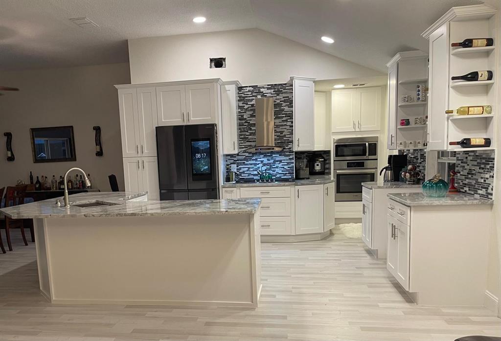 A modern kitchen features white cabinetry, a marble-topped island, and a mosaic tile backsplash — 167 GREELEY LOOP, DAVENPORT, FL