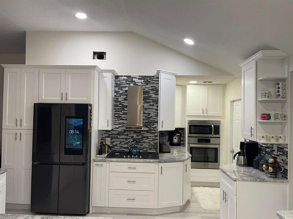 A modern kitchen features white cabinets, stainless steel appliances, a black refrigerator, and mosaic tile backsplash — 167 GREELEY LOOP, DAVENPORT, FL