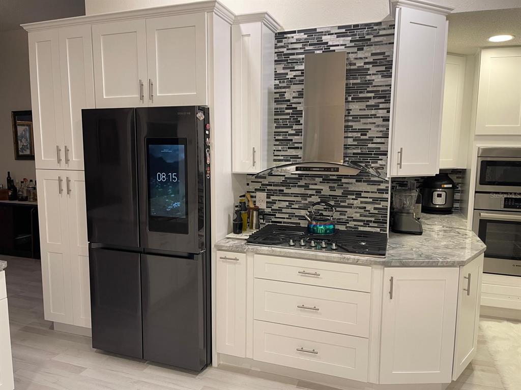 A kitchen features white cabinets, a black smart refrigerator, a gas cooktop, and mosaic backsplash — 167 GREELEY LOOP, DAVENPORT, FL