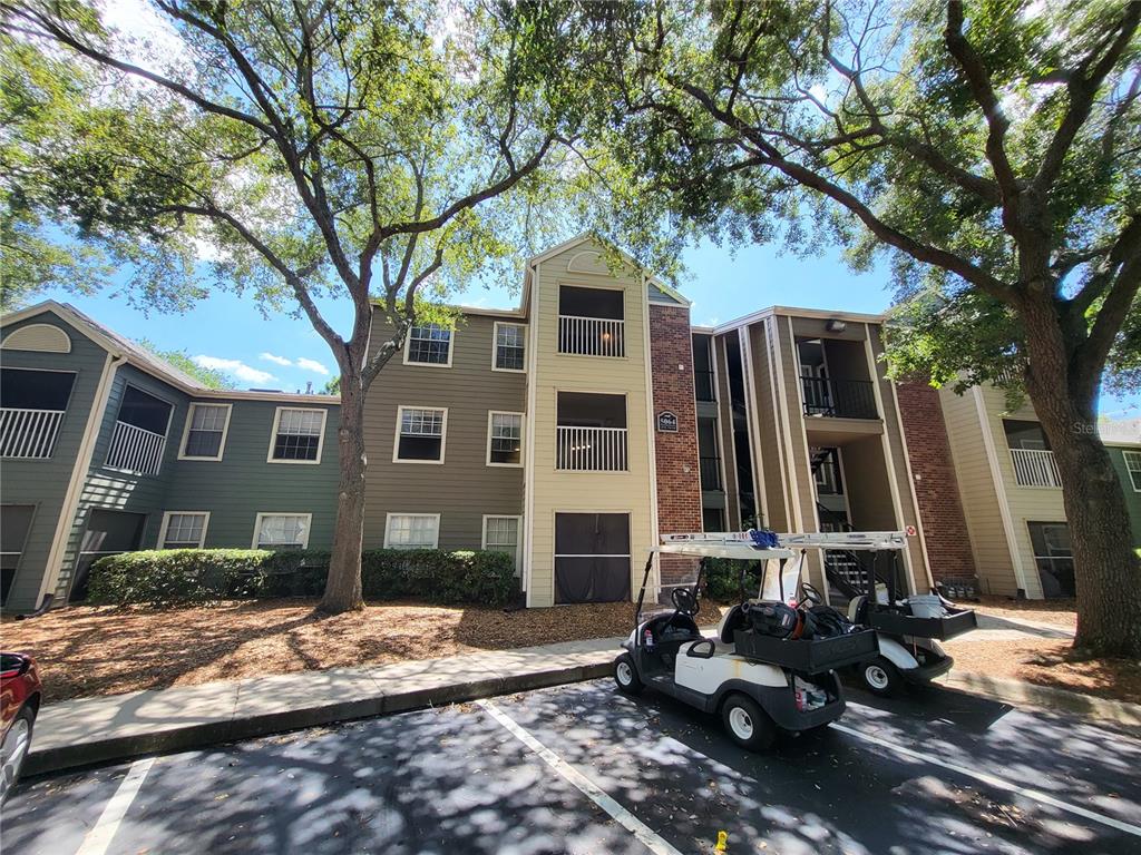 A three-story apartment building exterior features tan and green siding with two golf carts parked nearby — 5064 PARK CENTRAL DRIVE UNIT 1731, ORLANDO, FL