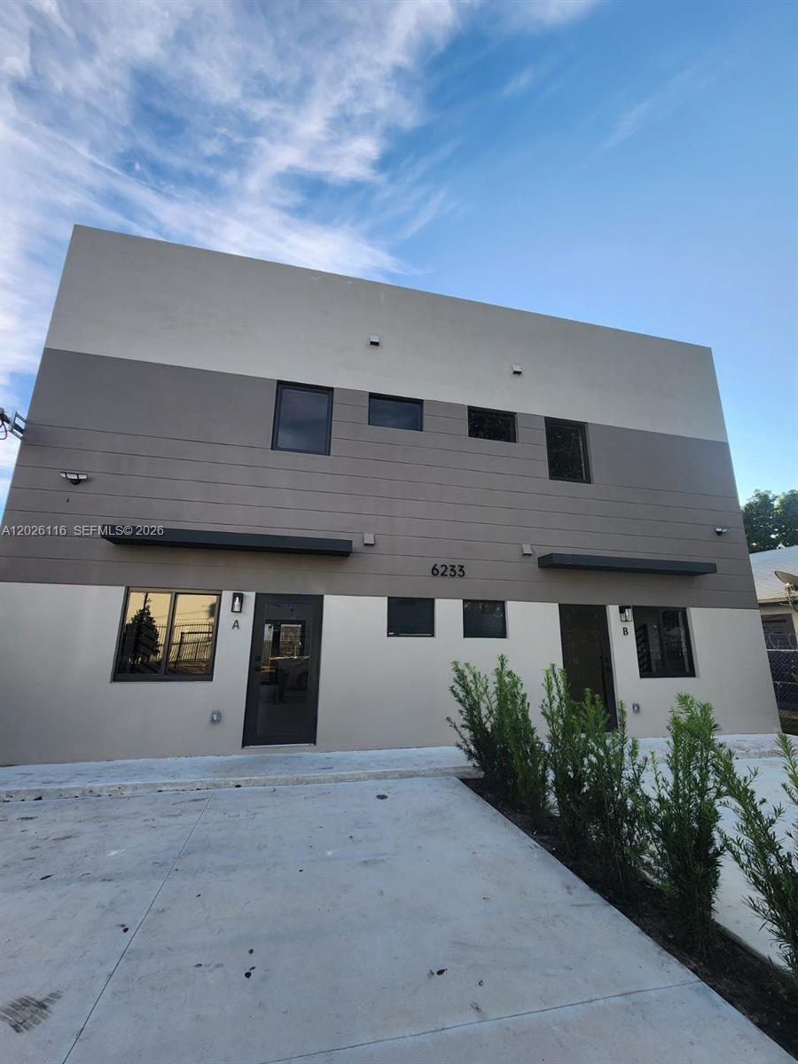 A two-story duplex building features a concrete driveway, modern gray siding, and two separate entrances — 6233 NW 20th Ave # B, Miami FL 33147, MIAMI, FL