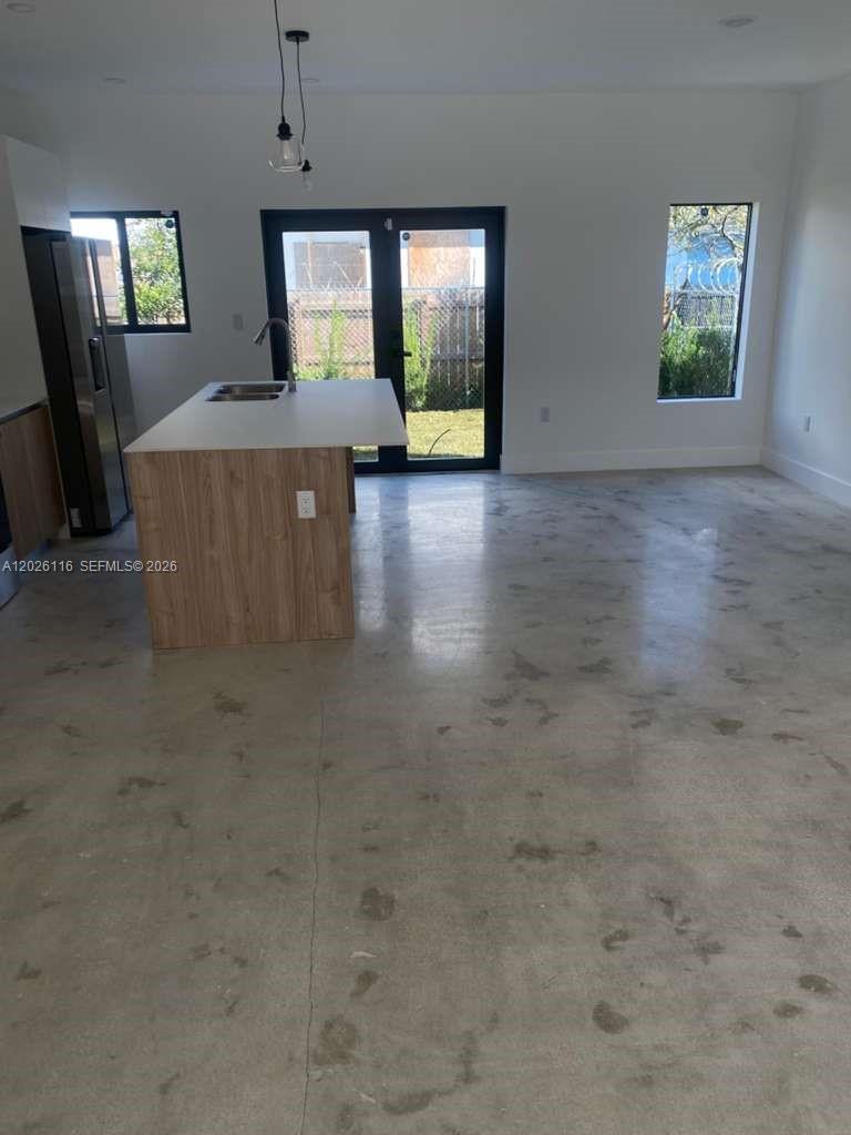 A kitchen with a wood-grain island and concrete floors opens to a backyard through doors — 6233 NW 20th Ave # B, Miami FL 33147, MIAMI, FL