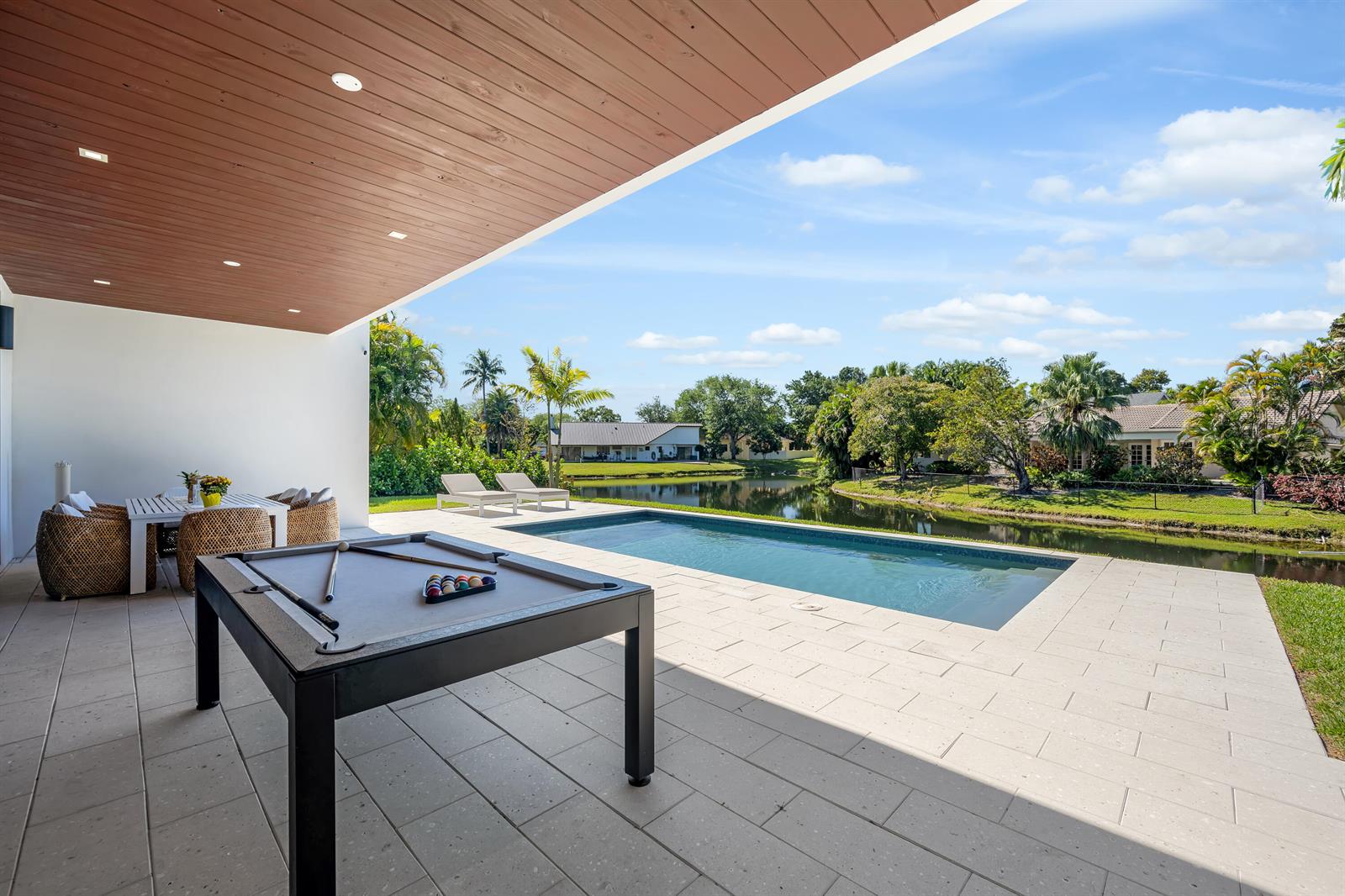 A covered patio features a pool table, dining area, and swimming pool overlooking a lake — 1000 SW 93rd Avenue, Plantation FL 33324, PLANTATION, FL