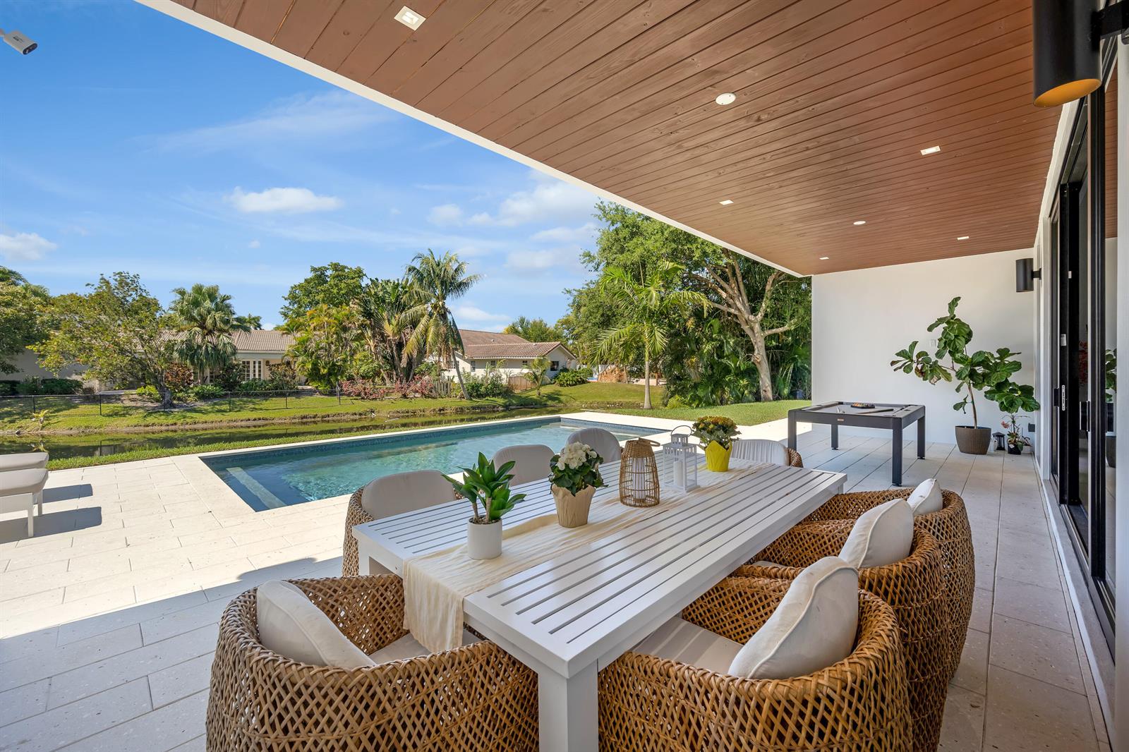 A covered patio features a white dining set, wicker chairs, and a pool overlooking a canal — 1000 SW 93rd Avenue, Plantation FL 33324, PLANTATION, FL