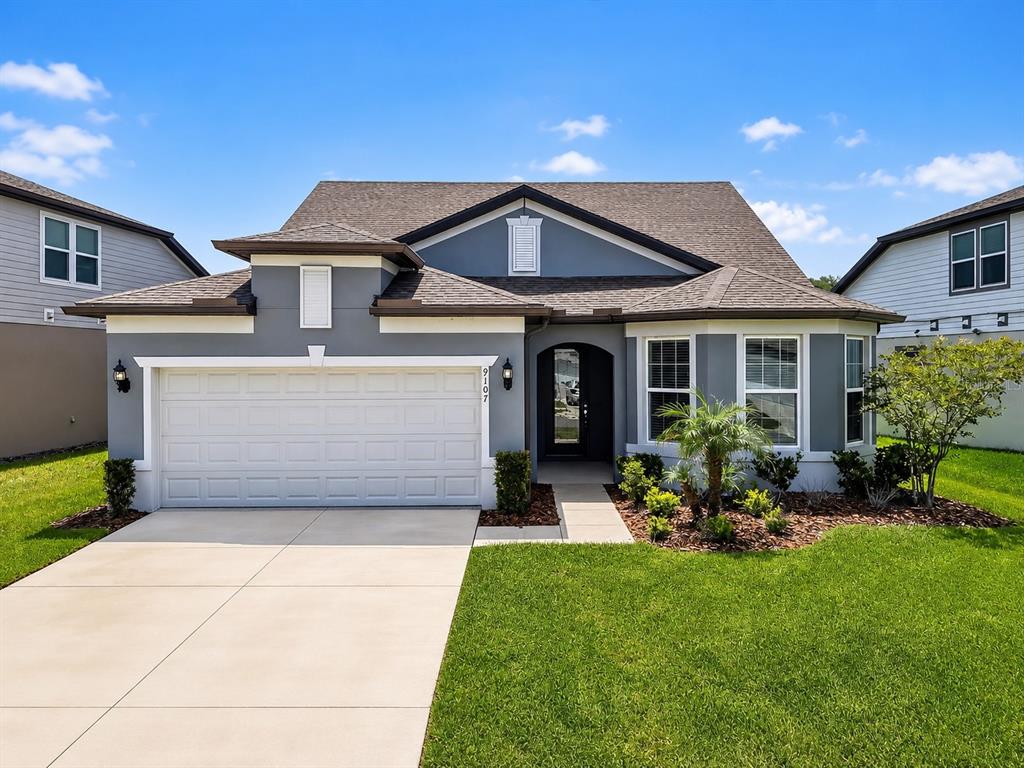 A single-story gray house with a two-car garage, a front porch, and a landscaped yard — 9107 RALLY SPRING LOOP, WESLEY CHAPEL, FL