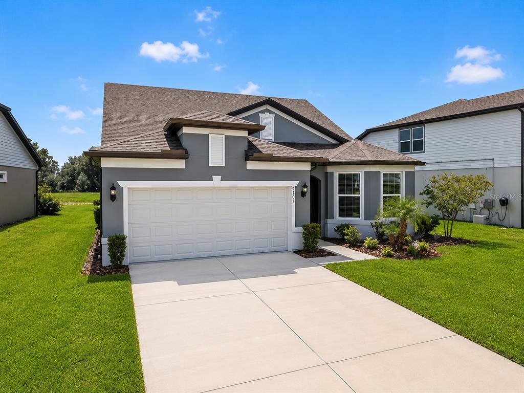 A gray single-story house with a two-car garage and a concrete driveway — 9107 RALLY SPRING LOOP, WESLEY CHAPEL, FL