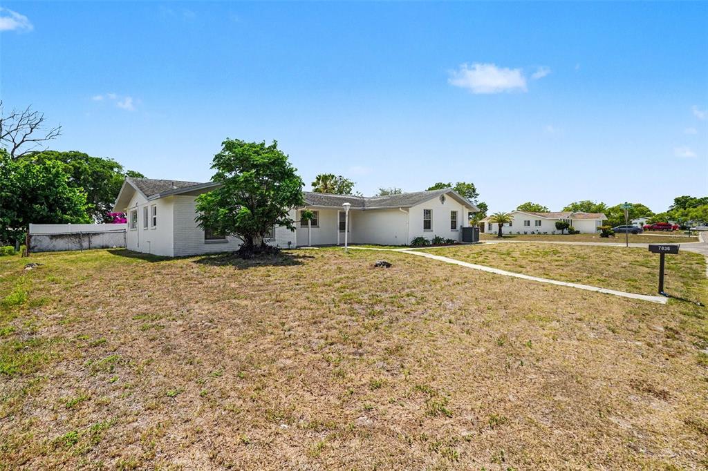 A white, single-story ranch-style house sits on a large, dry grass lot under a blue sky — 7836 LOTUS DRIVE, PORT RICHEY, FL