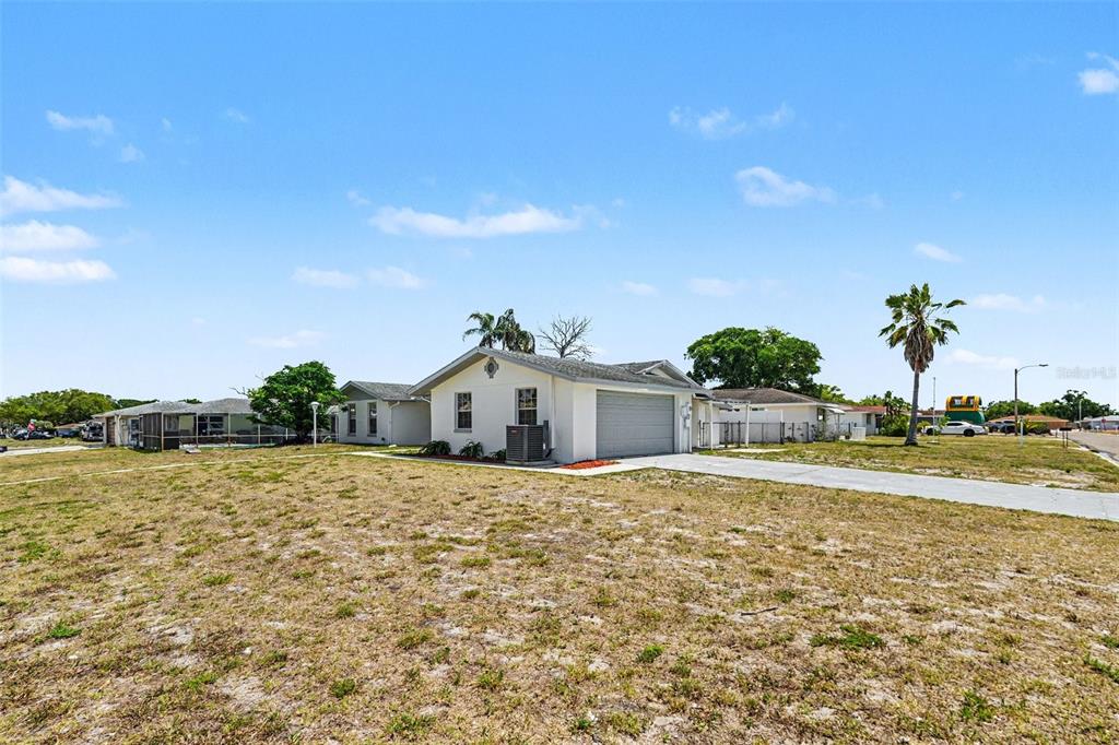 A single-story house with a garage and a large, dry grass yard under a blue sky — 7836 LOTUS DRIVE, PORT RICHEY, FL