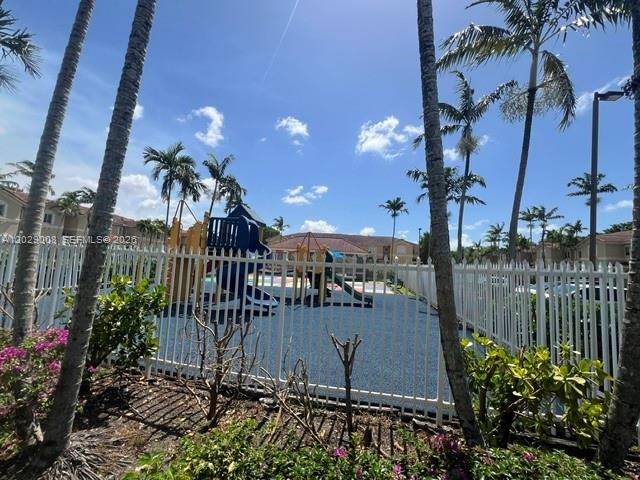 A fenced playground with a blue play structure sits under palm trees on a sunny day — 8258 NW 108th Pl # 4, Doral FL 33178, DORAL, FL