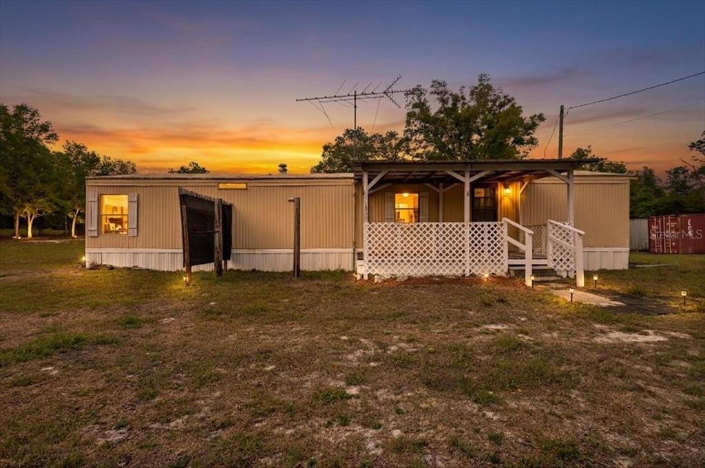 A single-story mobile home with a covered front porch and lattice railing at sunset — 3100 NW 20TH STREET, BELL, FL