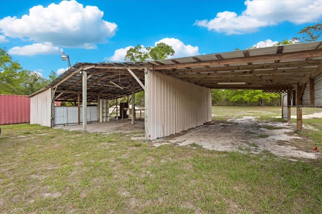 An open-sided metal pole barn structure sits on a grassy lot under a blue sky — 3100 NW 20TH STREET, BELL, FL