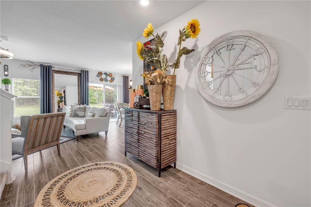 A foyer with wood-look tile flooring leads into a living room with a large mirror — 1105 PACIFIC DUNES COURT, DAYTONA BEACH, FL