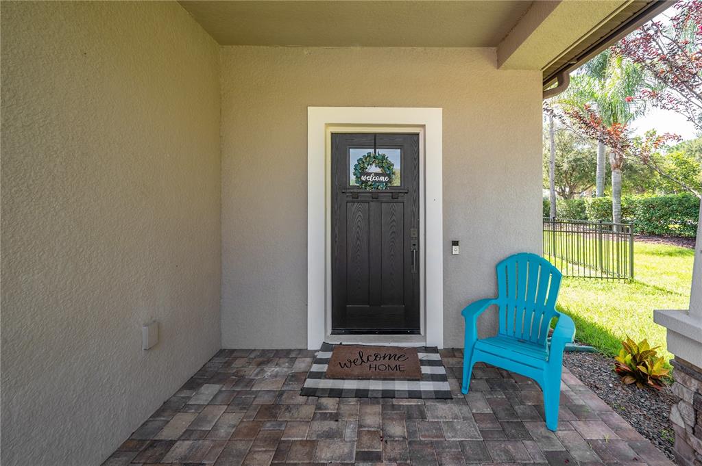 A dark front door with a wreath and a blue chair on a paved porch — 4342 O ROURKE COURT, WESLEY CHAPEL, FL