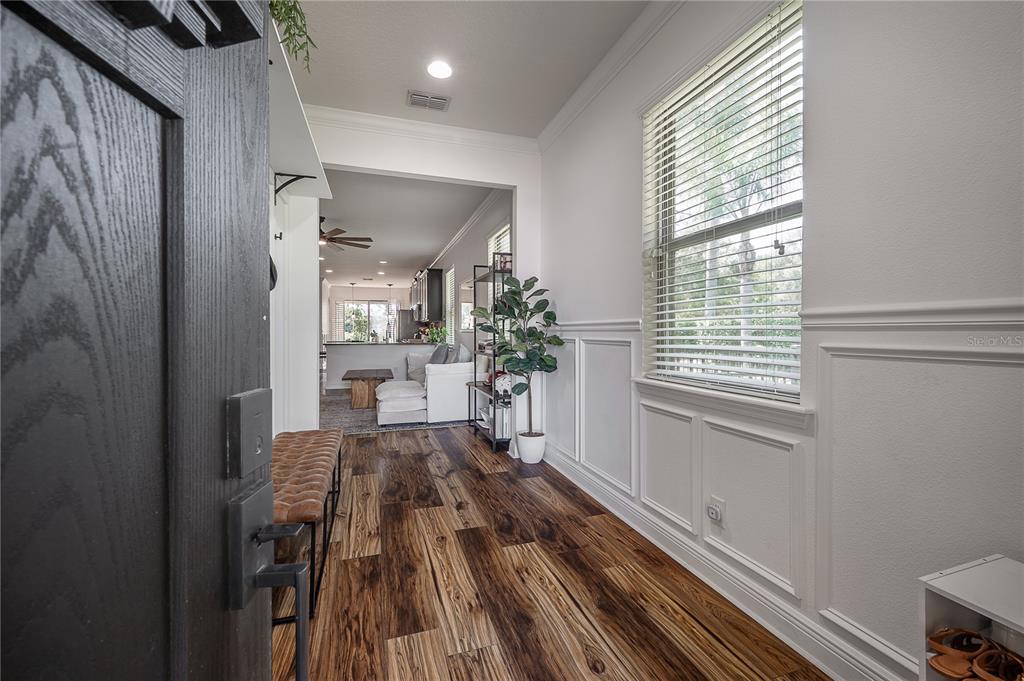 An entryway with wood-look flooring, wainscoting, and a bench leads into an open-concept living area — 4342 O ROURKE COURT, WESLEY CHAPEL, FL
