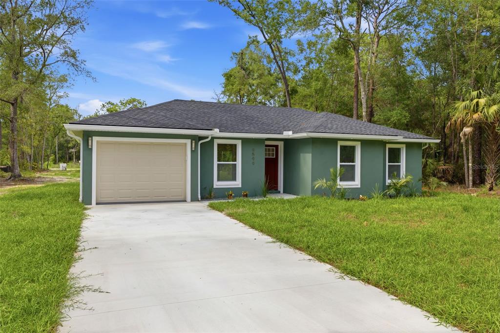 A single-story green house with a tan garage door and a red front door — 9599 W SANDRA STREET, CRYSTAL RIVER, FL