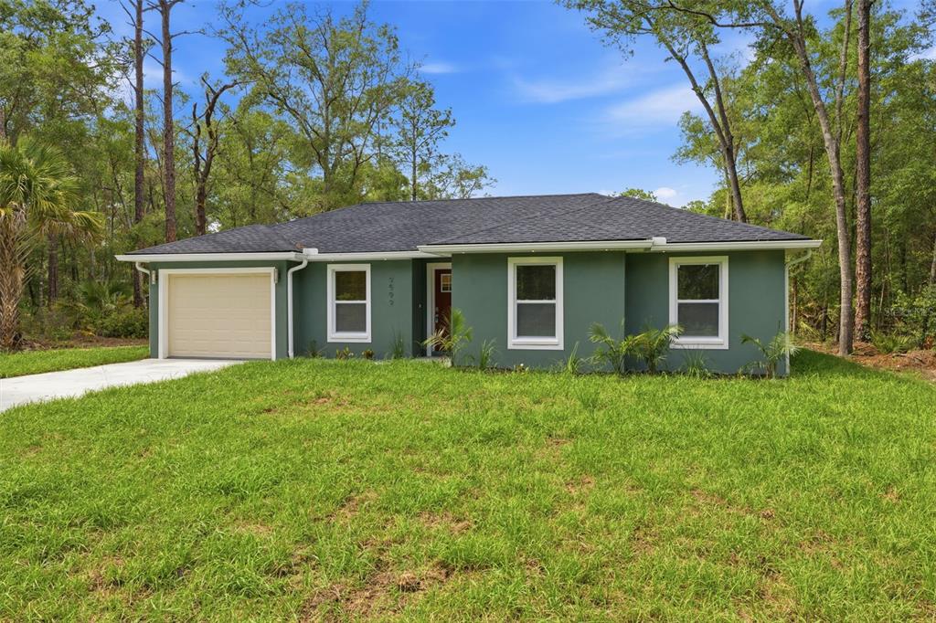 A single-story house with green stucco siding, a tan garage door, and a dark roof — 9599 W SANDRA STREET, CRYSTAL RIVER, FL