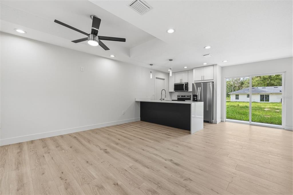 An open-concept kitchen and living area features light wood flooring, white cabinetry, and a sliding door — 9599 W SANDRA STREET, CRYSTAL RIVER, FL