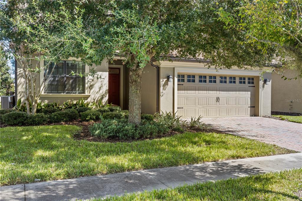 A single-story house exterior features a tan stucco facade, a two-car garage, and landscaping — 9117 EL CARO LANE, DAVENPORT, FL