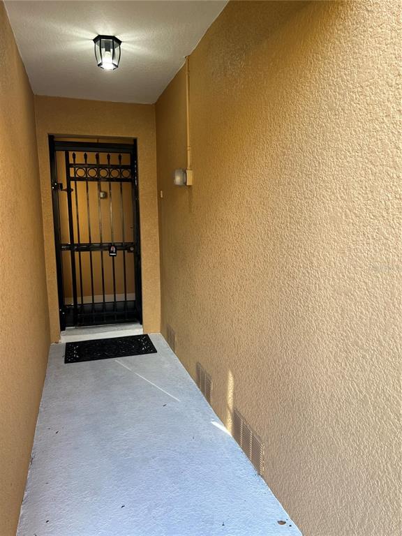 A narrow exterior entryway features a concrete floor, textured yellow walls, and a metal security gate — 5621 BLACKFIN DRIVE, NEW PORT RICHEY, FL