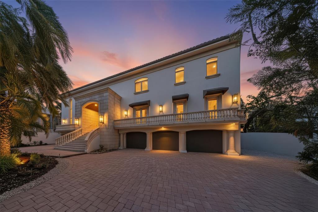 A multi-story house with a stone entryway, a balcony, and a three-car garage at dusk — 4136 ROBERTS POINT CIRCLE, SARASOTA, FL
