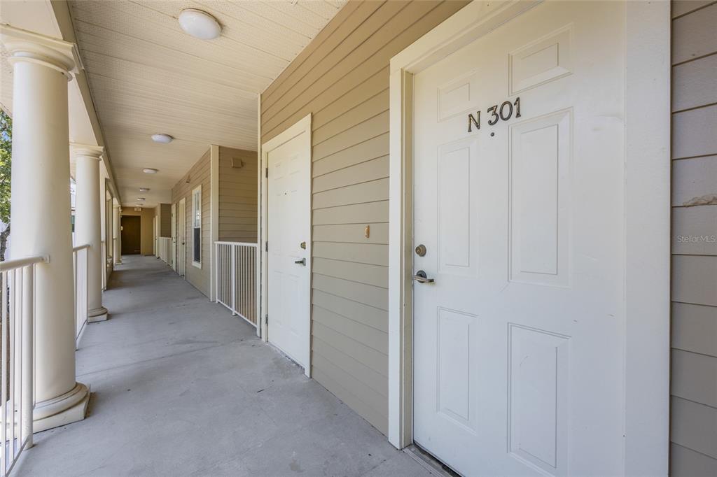 An outdoor apartment building walkway features white doors, beige siding, and white railings — 4941 SW 91ST TERRACE UNIT N301, GAINESVILLE, FL